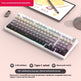 Mechanical keyboard with gradient keycaps on a light pink surface, tablet, and small car in the background.