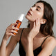 Woman holding a skincare bottle and touching her face against a neutral background