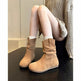 Bottes en daim beige portées par une personne assise sur une surface sombre avec un arrière-plan neutre