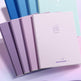 Set of pastel-colored notebooks with a visible brand logo on a light background