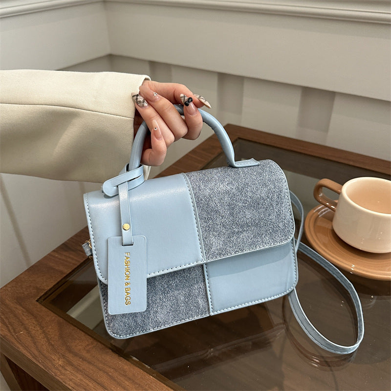 Hand holding a light blue handbag with glittery patch on a reflective surface.