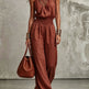 Woman wearing a rust-colored jumpsuit holding a matching handbag against a neutral background