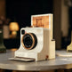 A retro-style instant camera in cream with bronze accents sits on a table, with a printed card emerging from the top slot and another card partially visible in the slot below.
