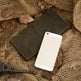 Brown leather wallet and white smartphone on a textured brown surface with leaves.