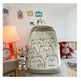 Backpack with cat designs on a bed with toys and a lamp in the background