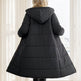 Person wearing a black puffer coat standing in a room with white curtains.