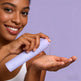 Woman holding a skincare product with a purple background