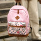Pink backpack with floral front pocket held by a person on a wooden staircase.