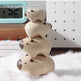 A stack of four small wooden pig toys with dark brown snouts and eyes, displayed on a white faux fur surface with a digital clock, books, and a white pegboard in the background.