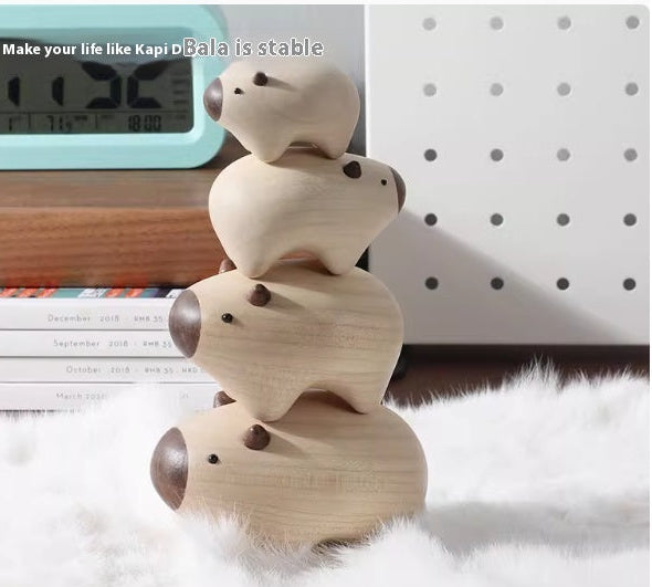 A stack of four small wooden pig toys with dark brown snouts and eyes, displayed on a white faux fur surface with a digital clock, books, and a white pegboard in the background.