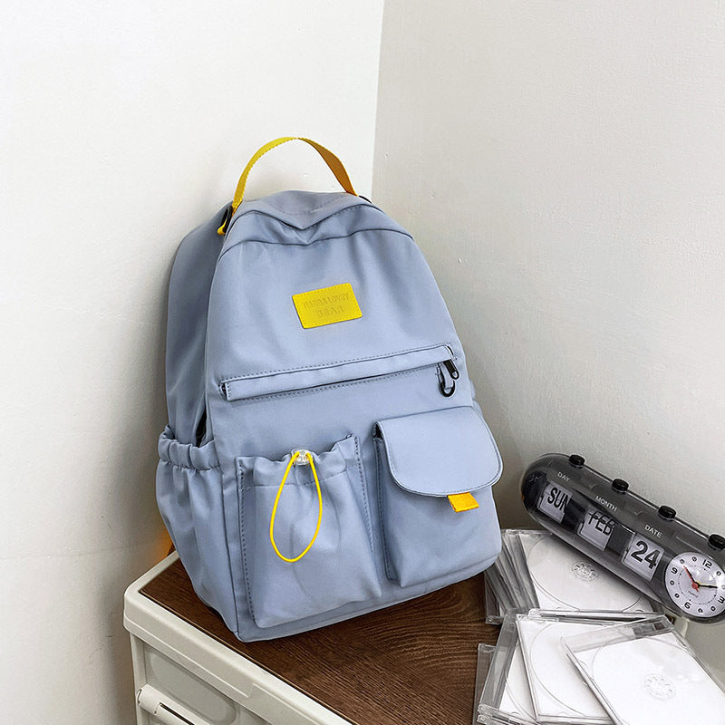 Light blue backpack with yellow accents on a wooden surface next to a clock and papers.
