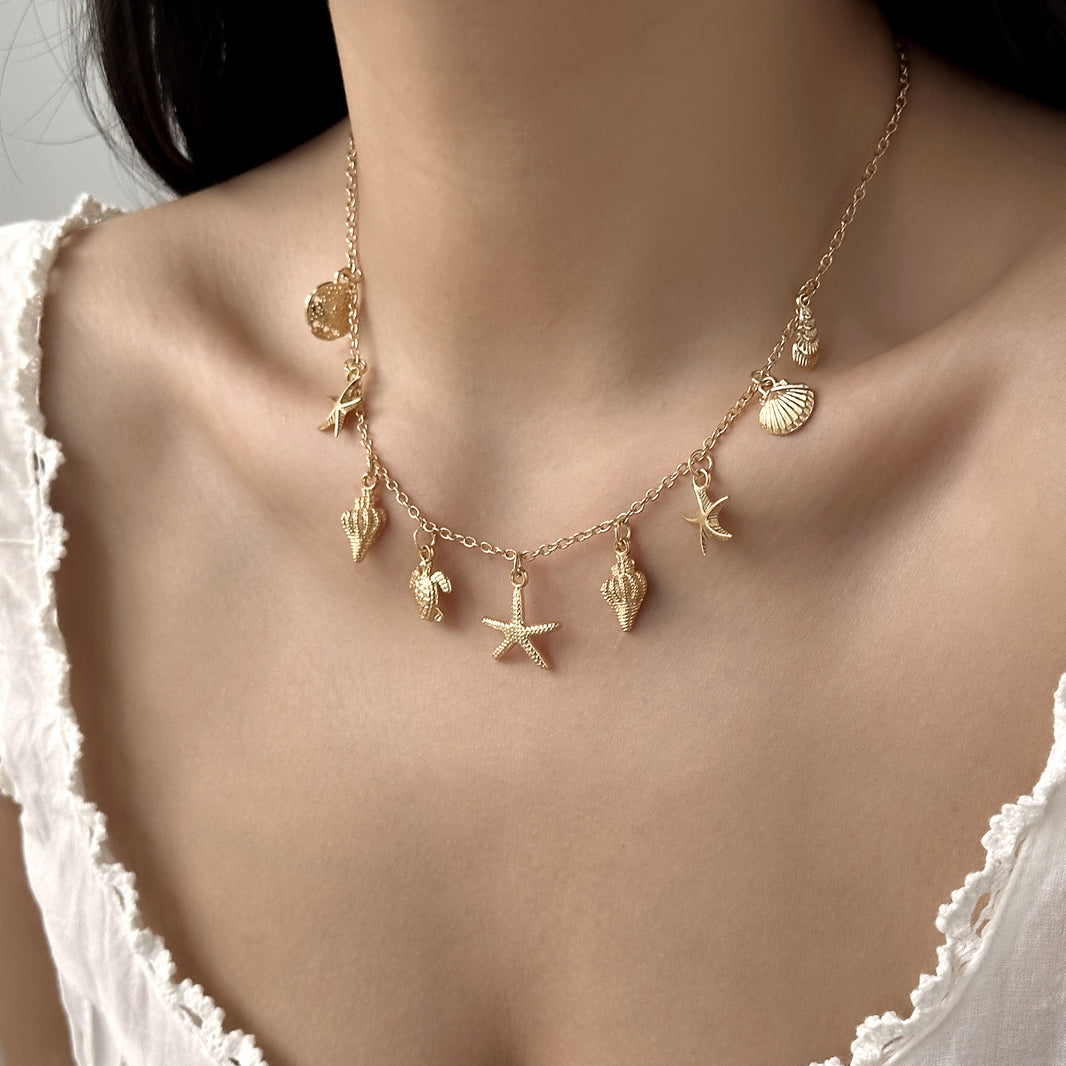 Gold necklace with starfish and shell charms on a model wearing a white lace top.