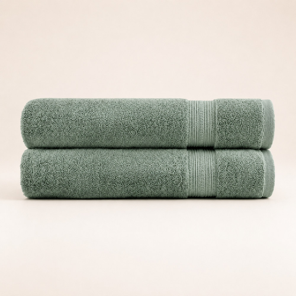 Two folded bath towels in a muted sage green color, stacked horizontally on a clean, solid, light beige background.